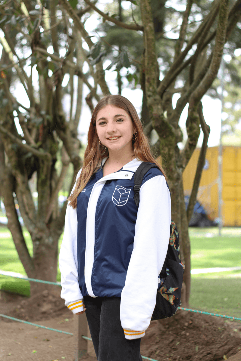 Estudiante de Comuna con la chaqueta institucional bajo los árboles